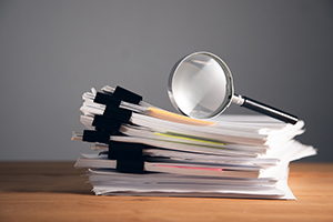 Eine Lupe liegt auf einem Stapel mit Dokumenten